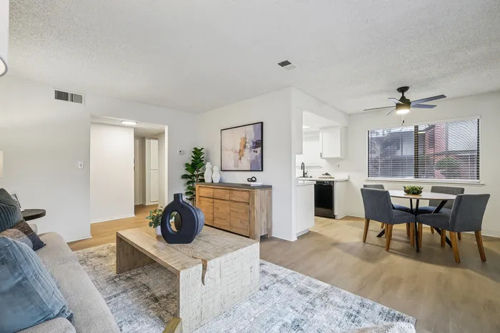 Bright and modern living area with stylish decor, featuring a cozy sofa, chic coffee table, and an open dining space next to large window with natural light.