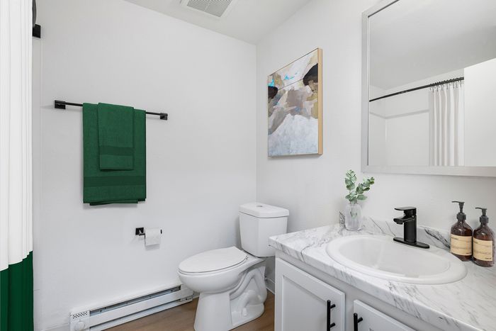 Modern bathroom with elegant marble countertop, sleek black fixtures, vibrant green towels, and contemporary artwork.