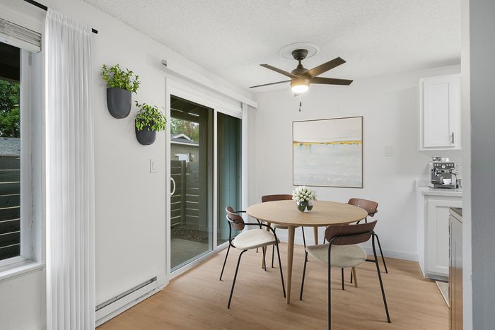 Bright dining area with elegant round table, modern chairs, and stylish wall art, featuring a serene garden view through sliding glass doors.