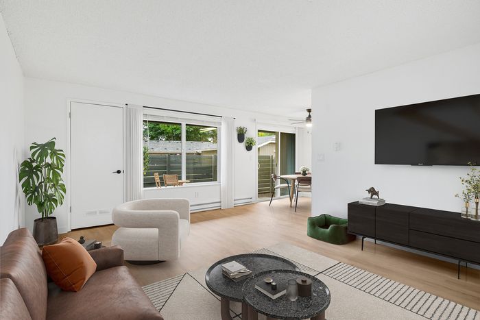 Bright, modern living room with sleek white walls, a cozy brown sofa, and a stylish TV setup. Features large windows and open space leading to a dining area, perfect for entertaining.