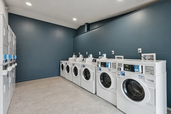 Modern laundry room with rows of high-efficiency washers and dryers against a sleek blue wall.