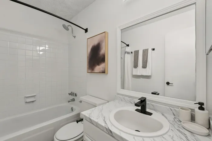 Elegant bathroom with a sleek white design, featuring a modern marble countertop, pristine bathtub, and stylish black fixtures.