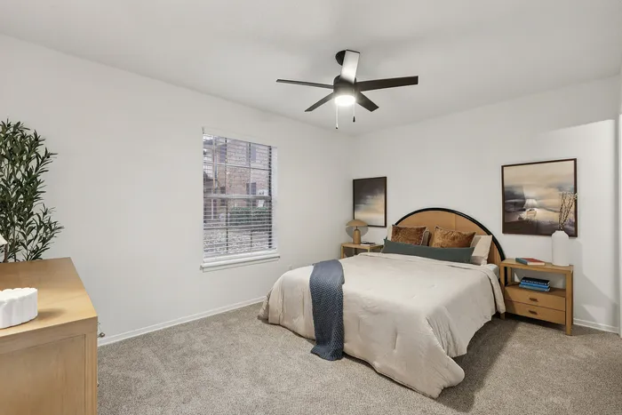 Inviting bedroom with luxurious bedding, modern ceiling fan, and elegant decor, providing a warm and tranquil atmosphere.