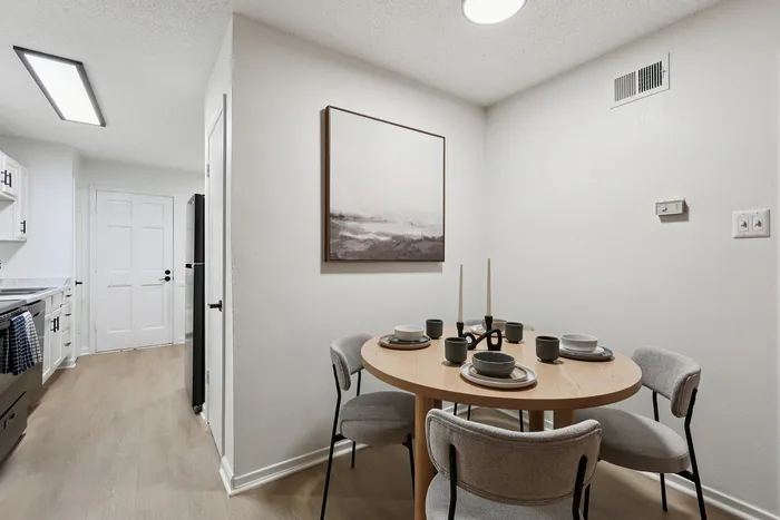 Chic dining corner with a round wooden table set for four, complemented by plush chairs and contemporary wall art.