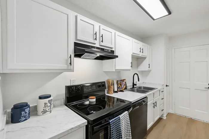 Modern kitchen with sleek white cabinets, marble countertops, and black appliances offering a sophisticated cooking space.