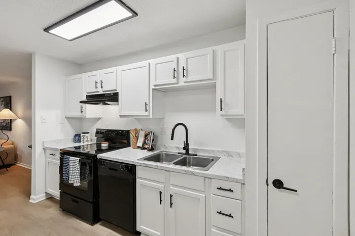 Modern kitchen with sleek white cabinetry, black appliances, and elegant marble countertops.