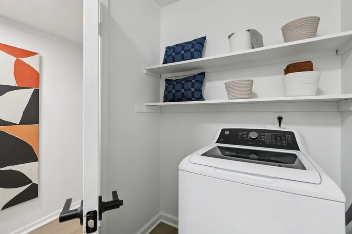 Modern laundry area featuring a sleek washer, open shelving with stylish baskets, and contemporary wall art.
