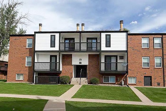Charming brick apartment building with balconies, nestled in a serene neighborhood with lush green lawns.