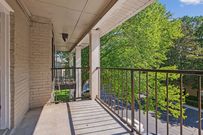 Charming balcony with brick accents and iron railing overlooking lush green trees, perfect for relaxation.