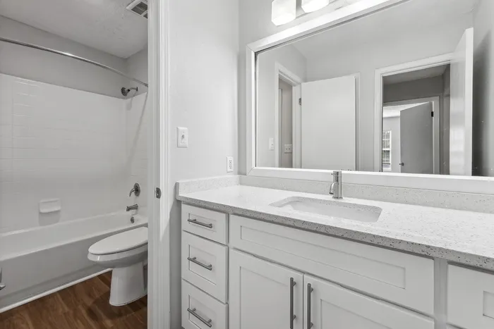 Modern bathroom with sleek white cabinetry, elegant countertop, and a well-lit mirror, offering a stylish and tranquil space.