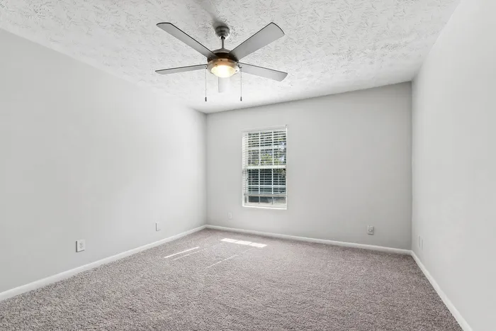 Bright and airy bedroom with soft carpet flooring, sleek ceiling fan, and large window offering ample natural light.