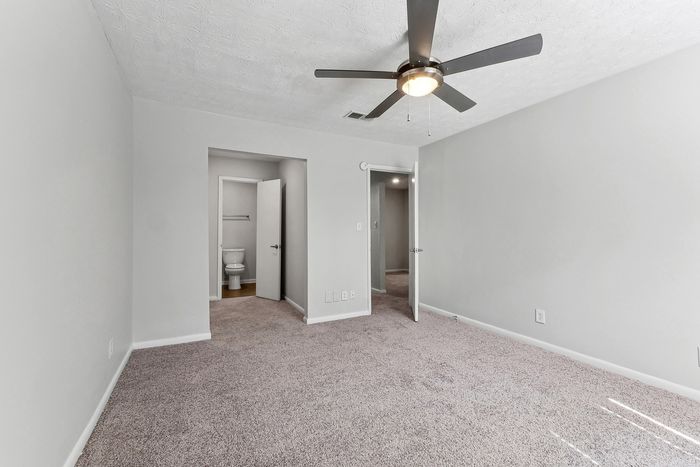 Bright and spacious bedroom with plush carpeting, ceiling fan, and an en-suite bathroom showcasing modern elegance.