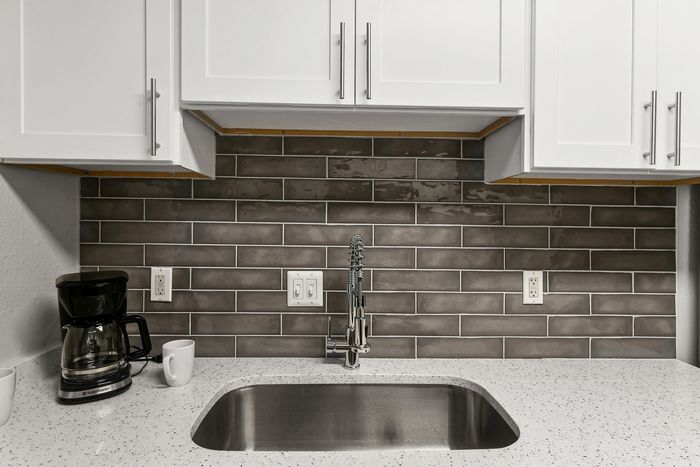Modern kitchen with elegant white cabinets, sleek gray subway tile backsplash, and a polished countertop featuring a built-in stainless steel sink and stylish faucet.