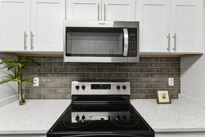 Modern kitchen with sleek stainless steel appliances, glossy black countertop stove, and elegant white cabinetry against a chic gray tiled backsplash.