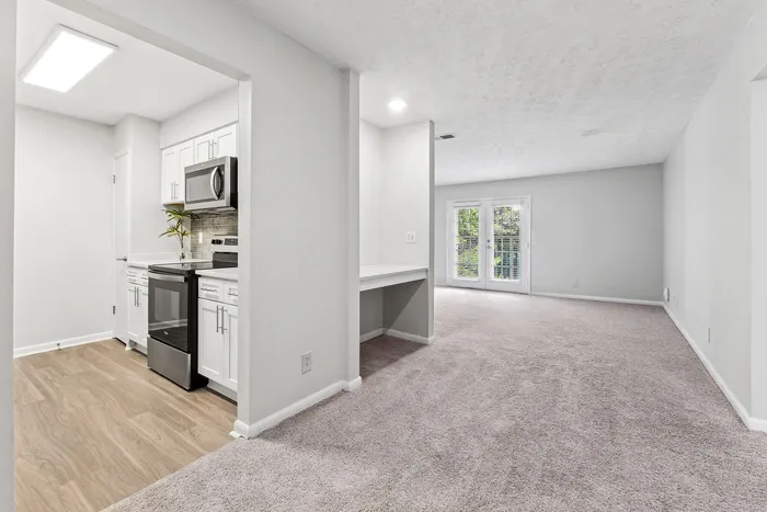 Bright and modern apartment showcasing a sleek kitchen with stainless steel appliances and an open, spacious living area filled with natural light from glass doors.