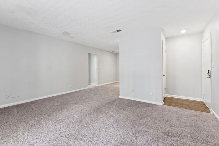 Bright and spacious room with plush carpeting, leading to an inviting hallway with soft natural light.