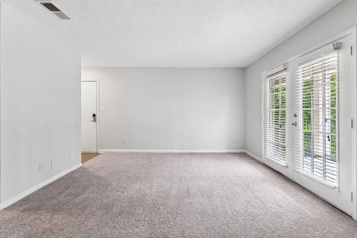 Inviting living room featuring plush carpet, French doors opening to natural light, and a bright, versatile space perfect for relaxation.