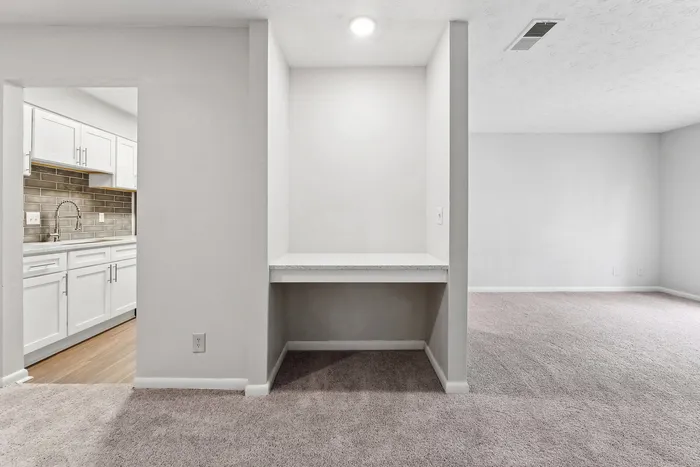 Sleek apartment interior featuring contemporary kitchen with stylish cabinetry, cozy carpeted living area, and a convenient built-in workspace.