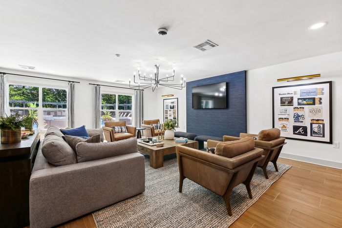 Spacious and stylish living room featuring a modern chandelier, elegant sofa, and large windows with garden views, perfect for relaxing and entertaining.
