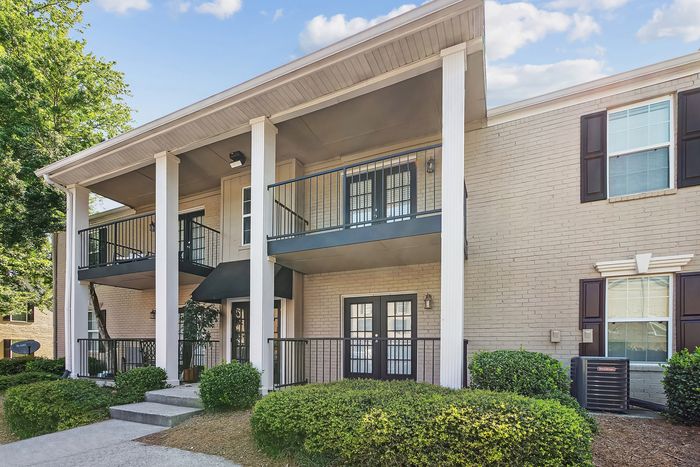 Charming two-story apartment building with elegant balconies, surrounded by lush greenery and beautiful landscaping.