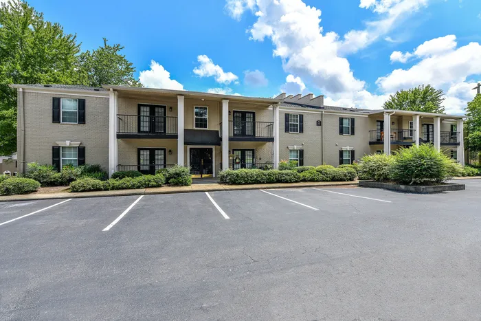 Charming two-story apartment complex with elegant balconies, nestled among vibrant greenery and set against a bright blue sky.