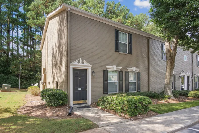 Charming two-story townhouse with elegant black shutters, surrounded by lush greenery and a tranquil setting.