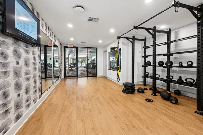 Modern apartment gym featuring sleek wooden floors, stylish decor, and a versatile array of fitness equipment including kettlebells, a TRX system, and more.