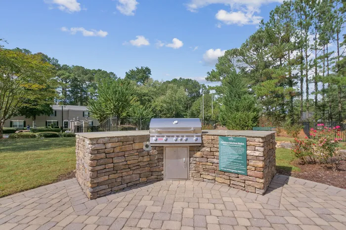 Charming outdoor grilling station in a lush communal area, surrounded by greenery and vibrant flowers, ideal for gatherings.