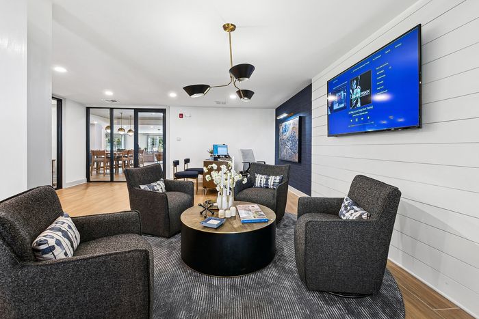 Chic and modern lounge area featuring cozy gray armchairs, a stylish round coffee table, and a large flat-screen TV, ideal for relaxation and entertainment.