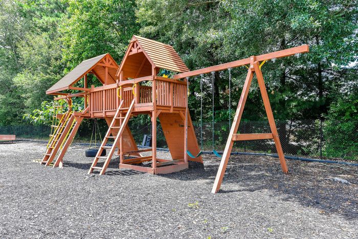 Inviting wooden playground set with swings and slides nestled in a lush green park, perfect for family-friendly fun.