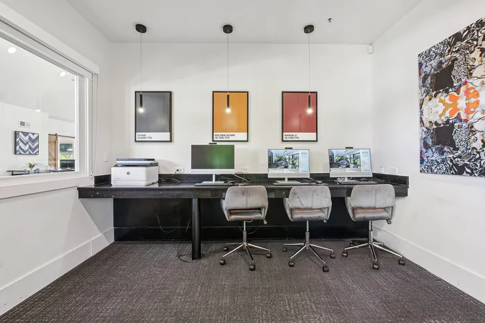 Modern communal workspace featuring sleek computer stations, vibrant wall art, and stylishly upholstered seating in a bright, sophisticated setting.