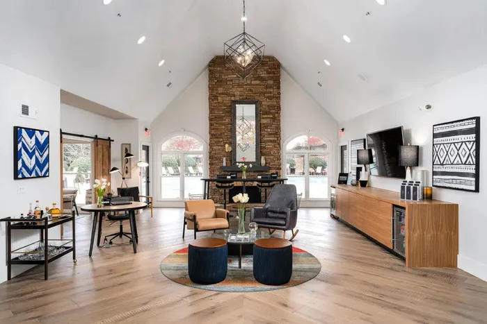 Elegant communal lounge featuring a vaulted ceiling, stone fireplace, stylish furniture, and floor-to-ceiling windows overlooking a pool.