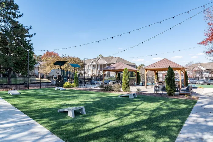 Charming apartment community with lush green space, inviting gazebos, and a modern playground under a clear blue sky.