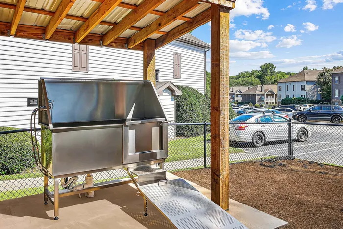 Modern outdoor pet wash station under a wooden pergola, featuring a sleek stainless steel design in a picturesque neighborhood setting.