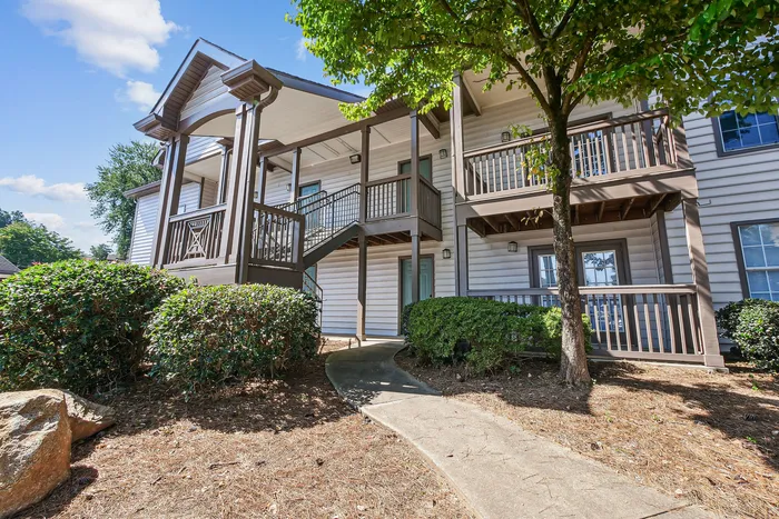Inviting apartment exterior with elegant two-story design, charming balconies, and lush greenery under a bright blue sky.