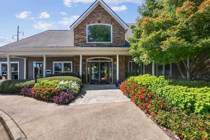 Charming residential building entrance surrounded by vibrant landscaping and lush greenery under a bright blue sky.
