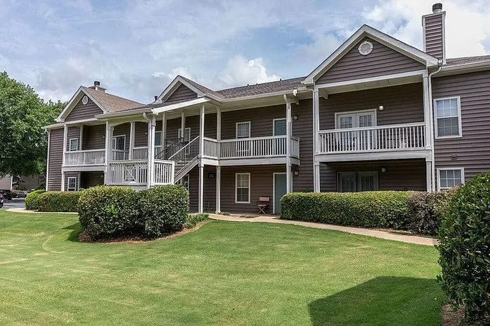 Charming apartment complex with elegant architecture, featuring spacious balconies, surrounded by lush greenery and a well-maintained lawn.