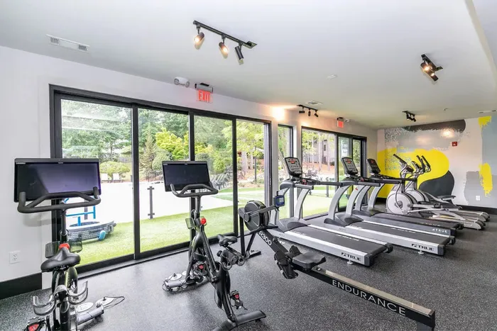 Modern fitness center with large windows, state-of-the-art exercise bikes, and treadmills overlooking a lush green outdoor space.