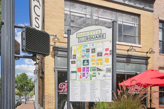 Vibrant outdoor scene of Marietta Square with a detailed map, charming brick building, and bright red patio umbrellas.