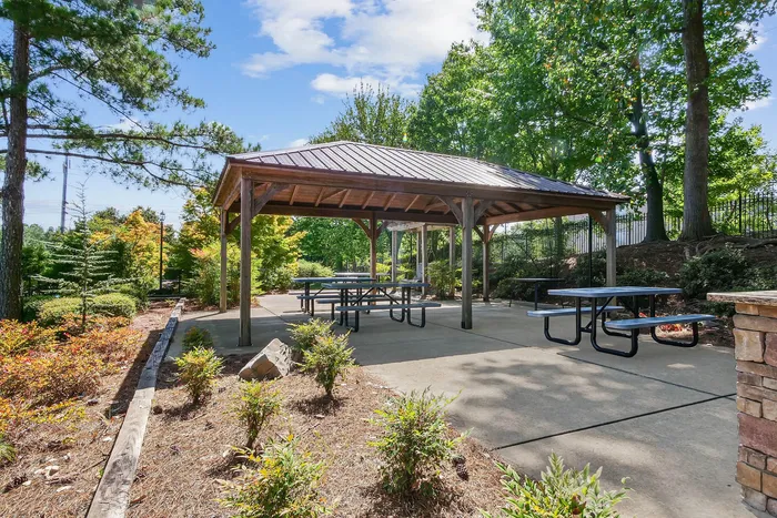 Charming outdoor gazebo in a lush green garden, featuring picnic tables perfect for gatherings and relaxation.