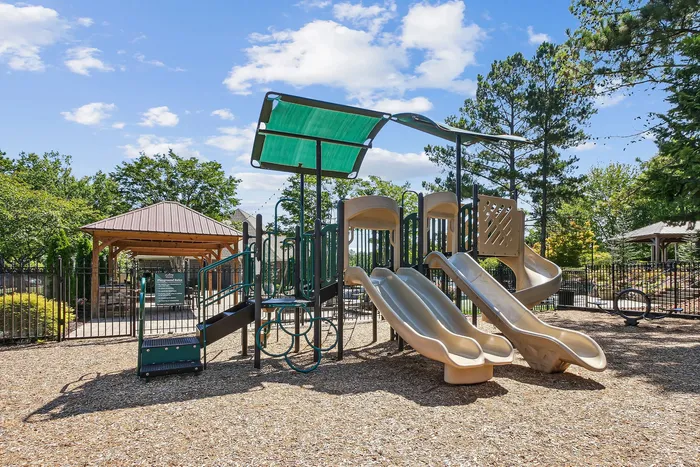 Inviting playground area in a lush residential community, featuring slides and climbing structures under a sunny sky.