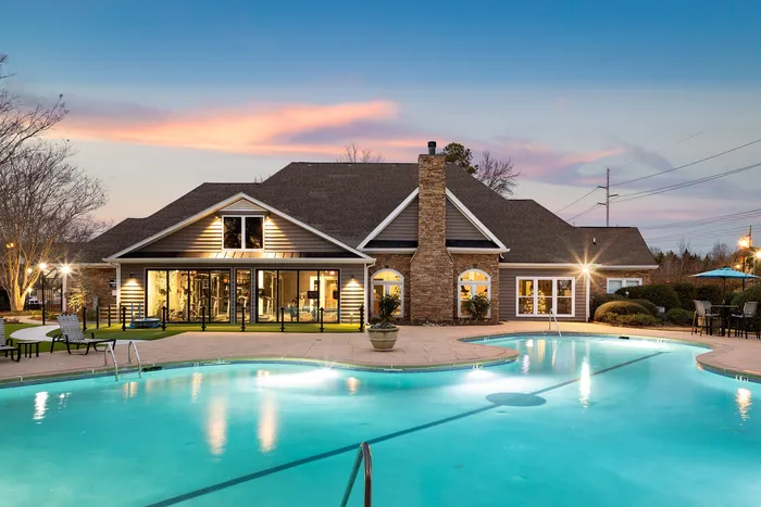 Charming evening view of a luxurious clubhouse with glowing pool, inviting outdoor seating, and beautiful sunset sky.
