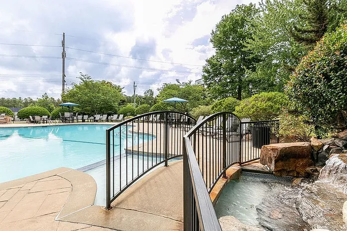 Elegant poolside area featuring a charming footbridge, cascading waterfall, and lush greenery, offering a tranquil outdoor retreat.