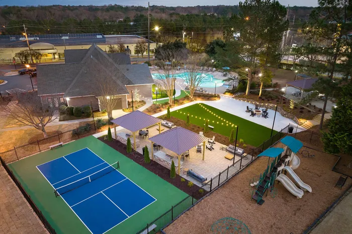 Charming apartment complex featuring a tennis court, illuminated pool area, cozy gazebos, and a playful children&rsquo;s playground, set amidst lush greenery.