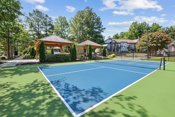 Inviting apartment complex featuring a fresh tennis court surrounded by lush greenery and charming wooden gazebos, perfect for active living and relaxation.