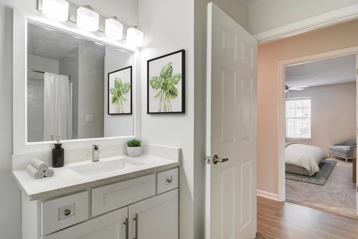 Chic bathroom with modern vanity, framed botanical art, and peek into a cozy bedroom, offering elegance and comfort.