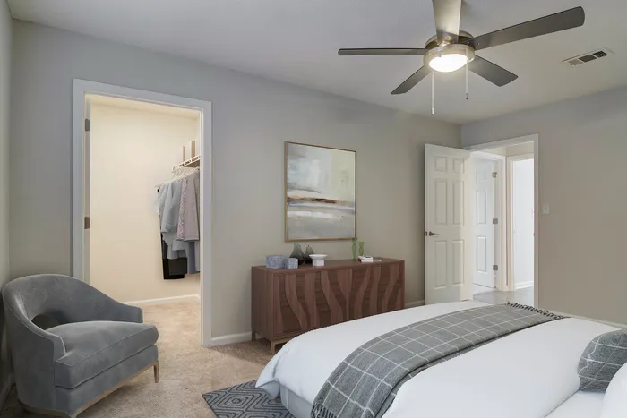 Inviting bedroom with modern decor, featuring a cozy gray chair, elegant dresser, and a spacious walk-in closet with stylish clothes organization.