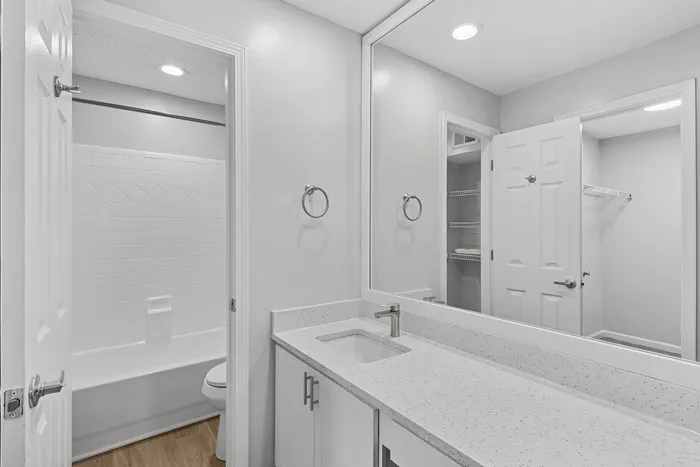 Sleek and modern bathroom with elegant white countertops, a spacious mirror, and pristine fixtures, ideal for stylish apartment living.