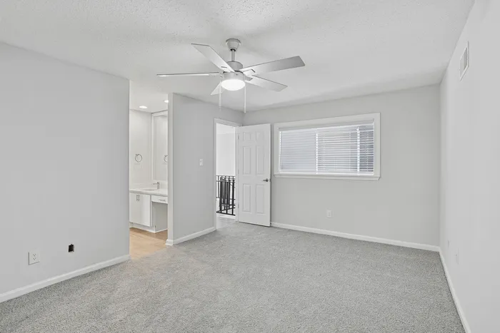 Bright and airy bedroom with a sleek ceiling fan, plush carpeting, and an en-suite vanity area.