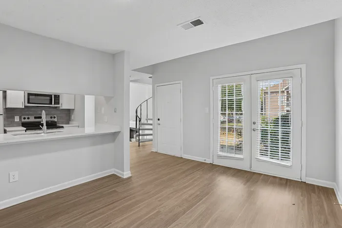 Bright and inviting living space featuring sleek wood floors, a modern kitchen with stainless steel appliances, and elegant French doors overlooking a charming outdoor view.
